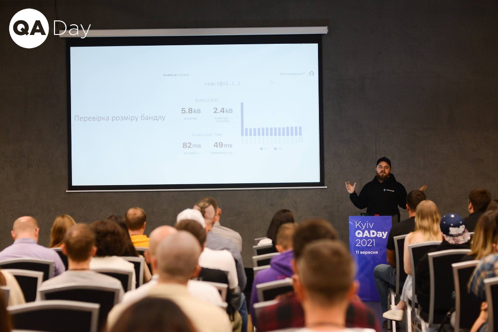 Oleksandr Khotemskyi speaking to a full hall at Kyiv QA Day 2021, next to a slide about checking JavaScript bundle size.